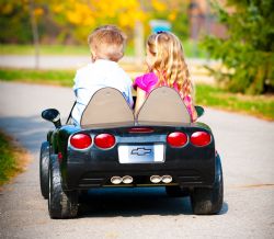 children riding in motorized toy car along sidewalk.